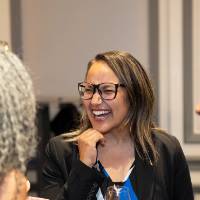 Woman holding her hand under her chin while laughing at conversation with other event guest